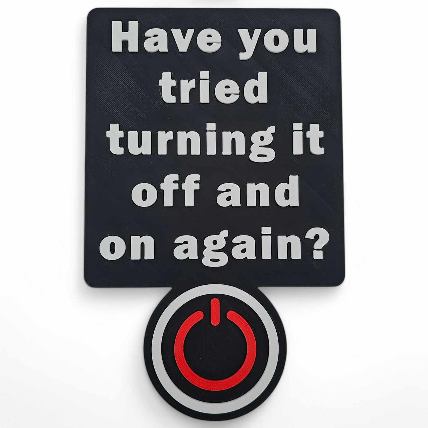 3D printed black tech sign with raised white text "Have you tried turning it off and on again?" and a red and green power button icon.