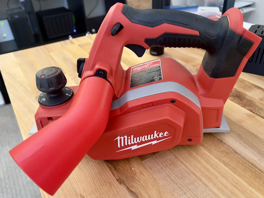 Milwaukee 2623-20 planer with red chip deflector attached to exhaust port on wooden surface