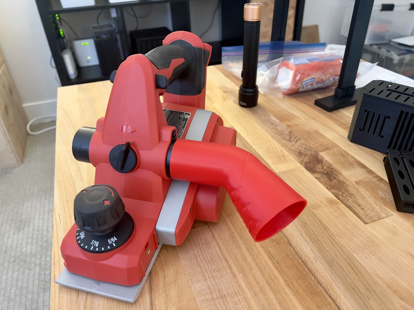 Milwaukee 2623-20 planer with red chip deflector attached to exhaust port on wooden workbench.