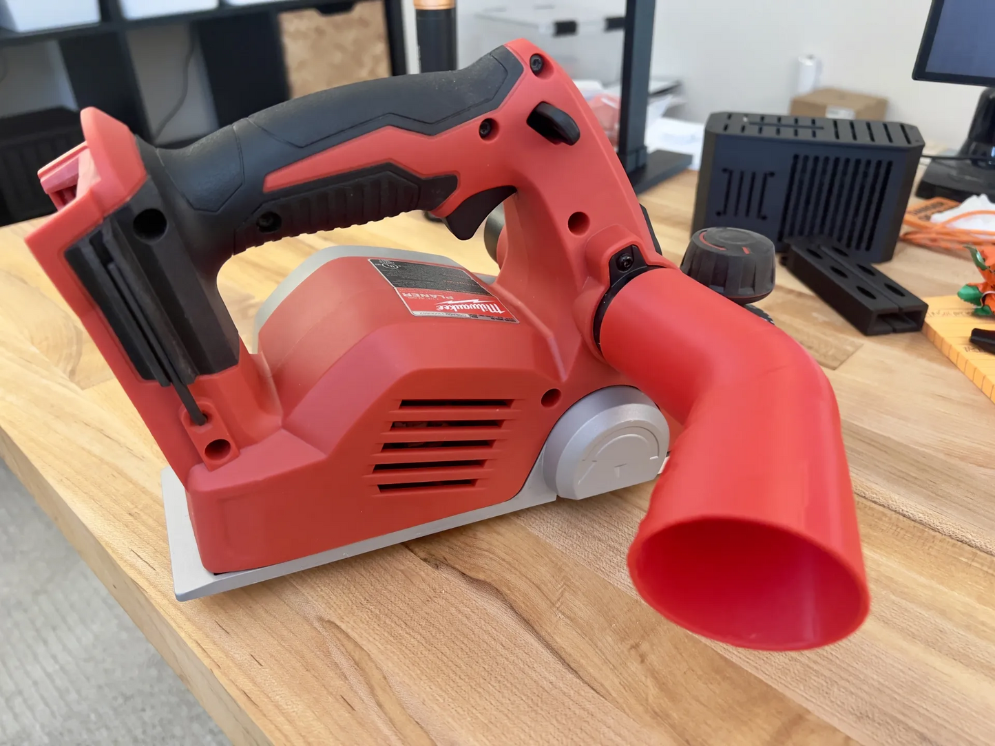 Milwaukee 2623-20 planer with red chip deflector attached to exhaust port on wooden workbench