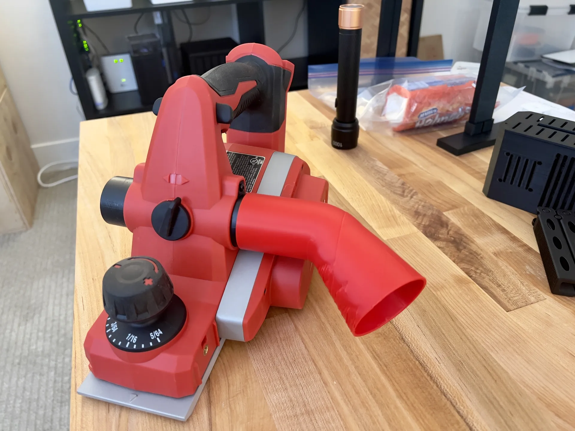 Milwaukee 2623-20 planer with red chip deflector attached to exhaust port on wooden workbench.